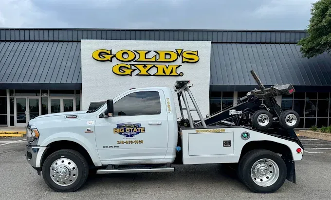 A white Mid-State tow truck parked in front of a Gold's Gym building.