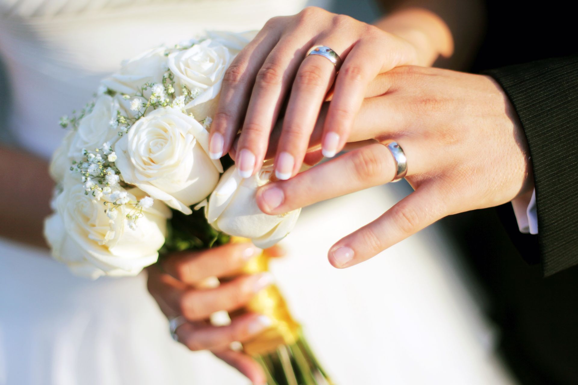 Wedding rings on hands over a white rose bouquet.