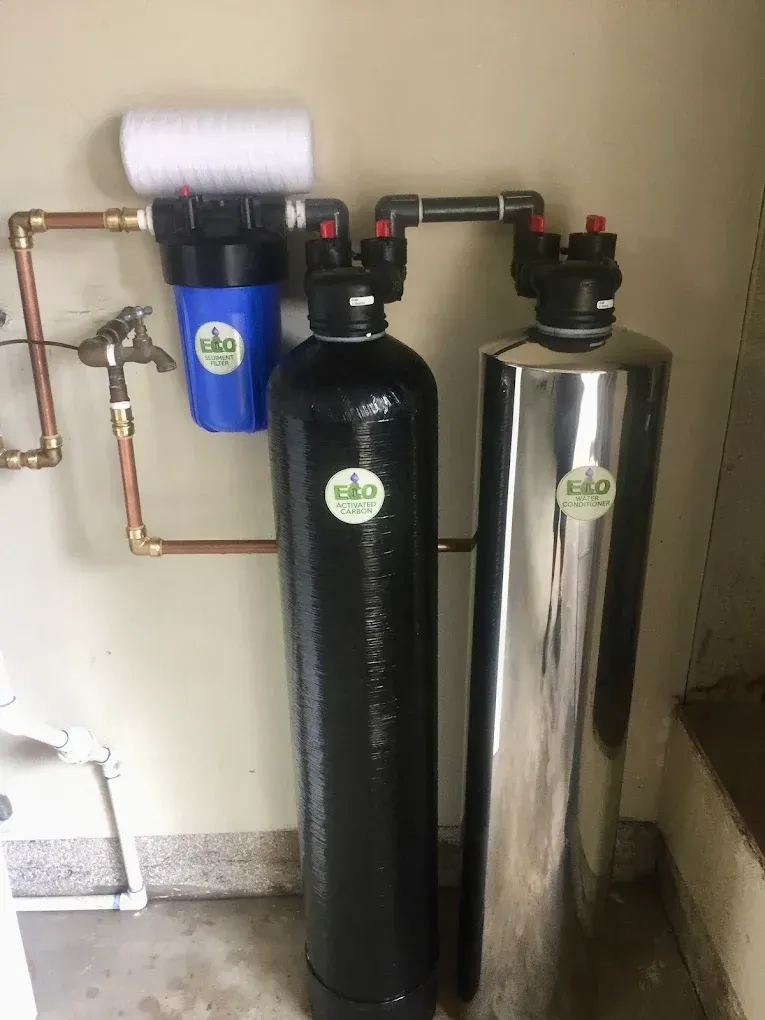 Water filtration system with three tanks and copper piping, mounted on a beige wall.