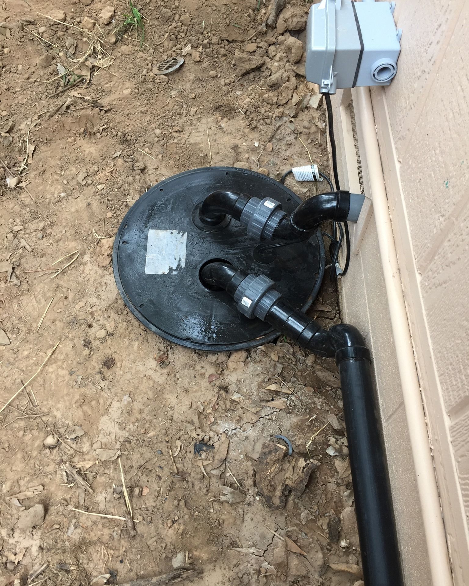Black pool filter with pipes, ground, and electrical box on a wall.