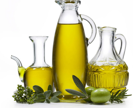 Three glass oil bottles with olive oil, surrounded by green olives and herbs.