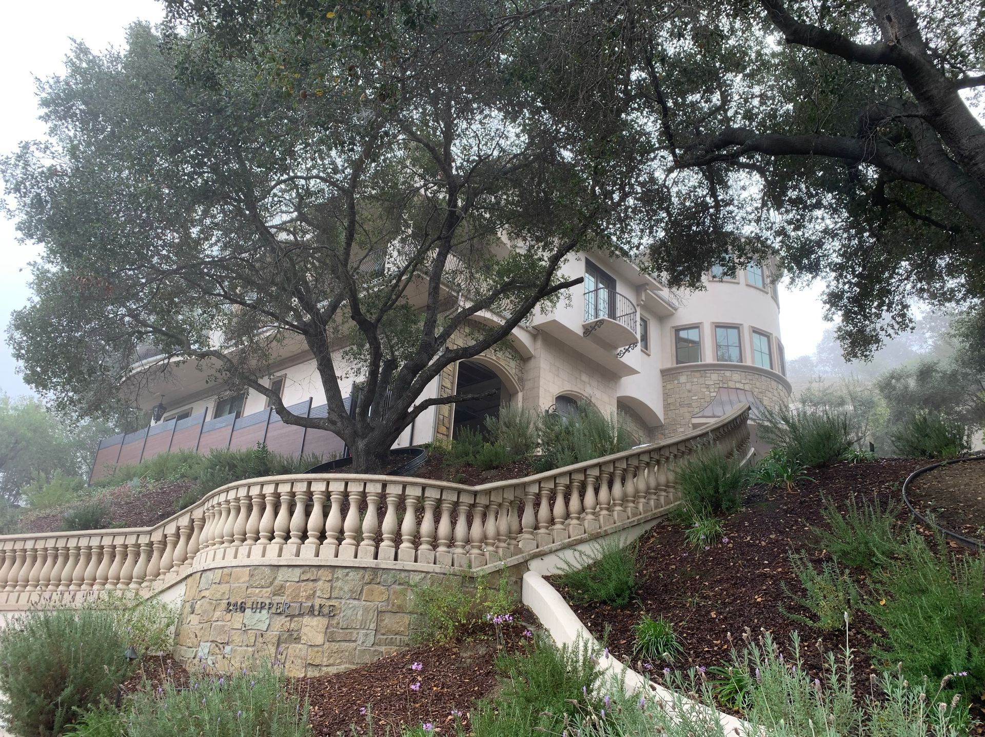 Large house on a hill, obscured by fog, with a stone facade, a curved balcony, and a balustrade.