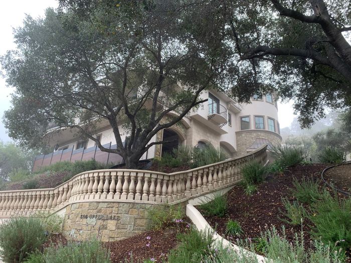 Large house on a hill, obscured by fog, with a stone facade, a curved balcony, and a balustrade.