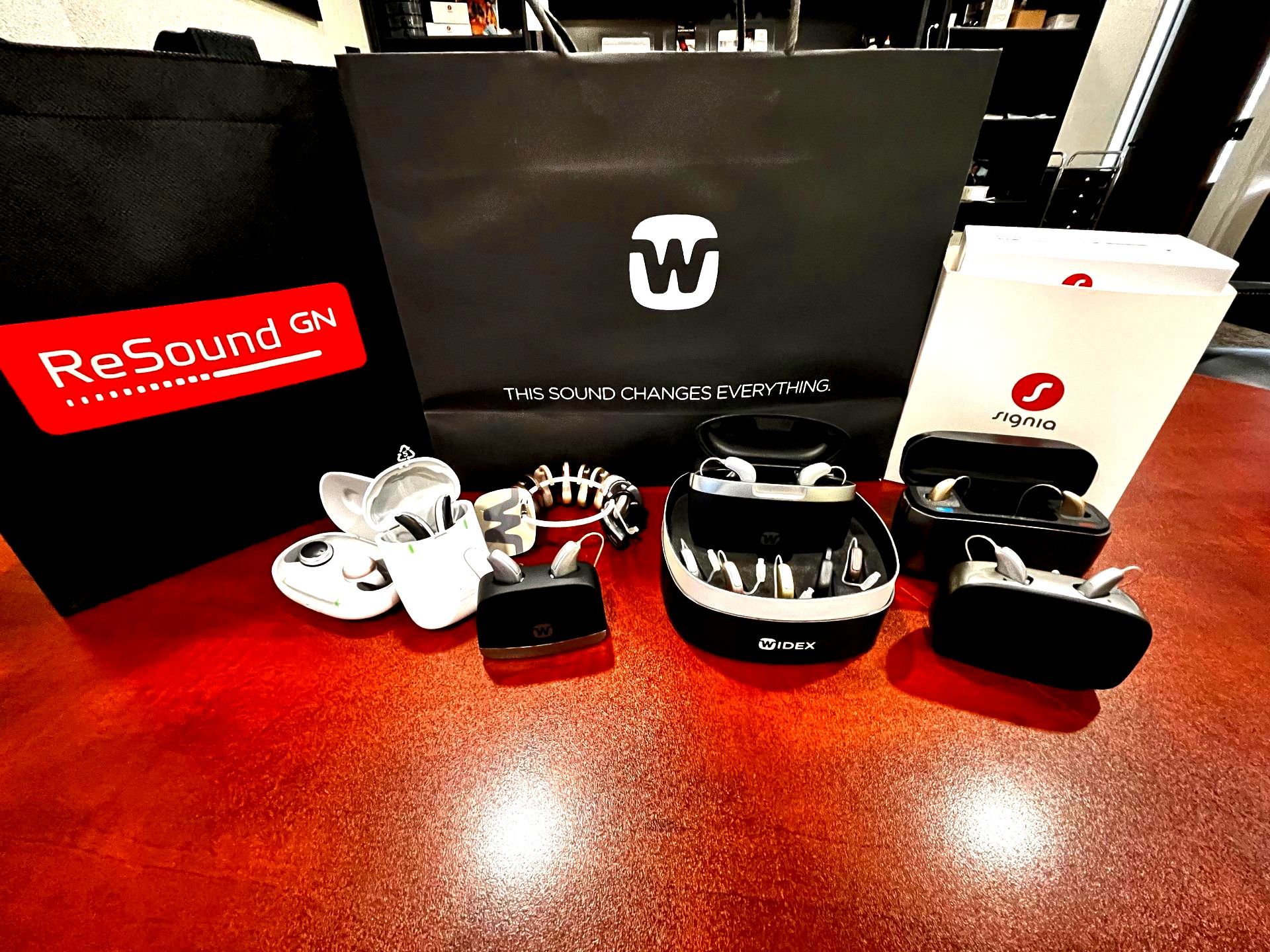 Items related to hearing aids on a red surface. Includes bags, a charger, and hearing aids.