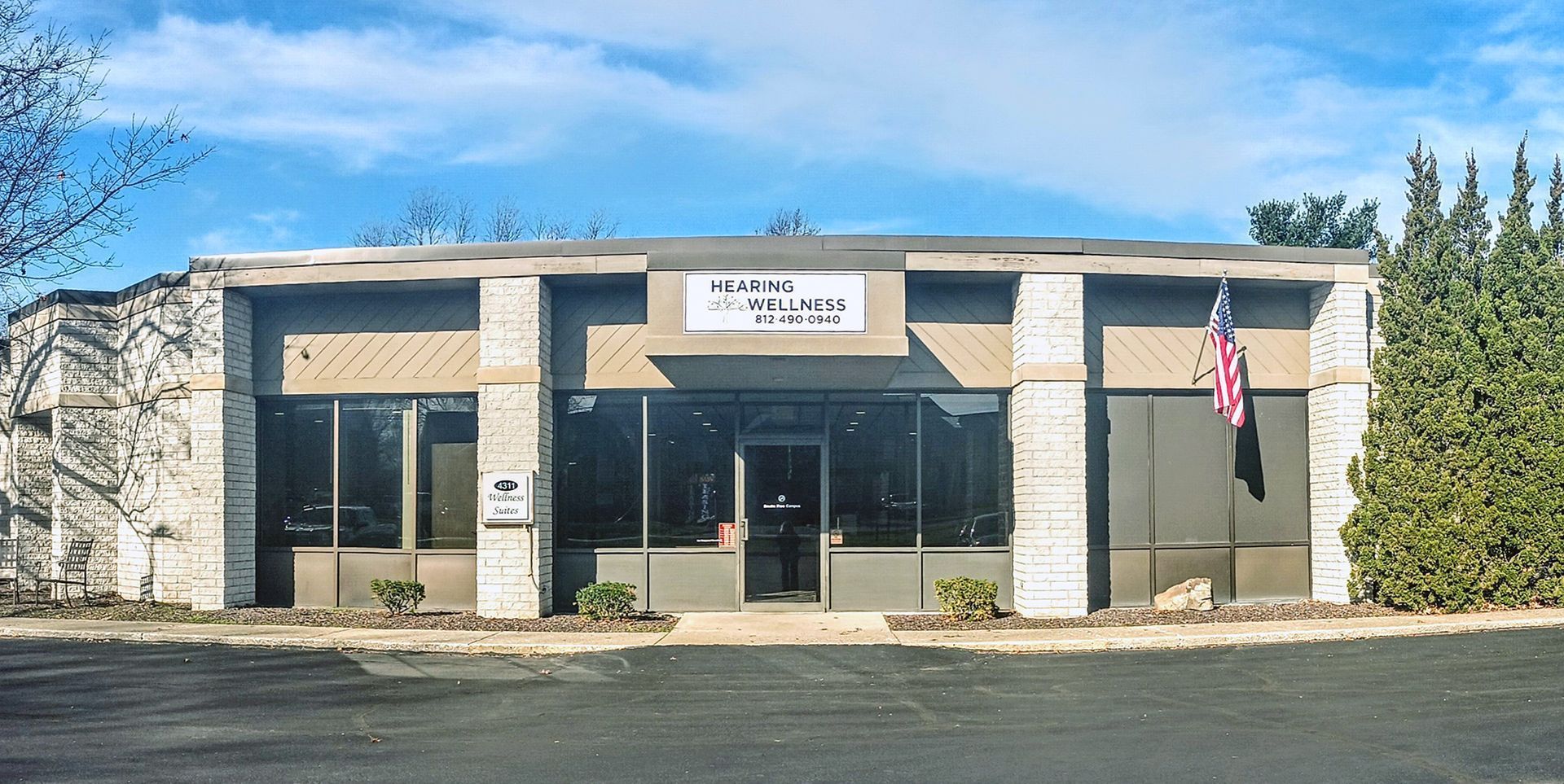 A building with a stone facade has a centered entrance and windows, reads Hearing Wellness on the front.
