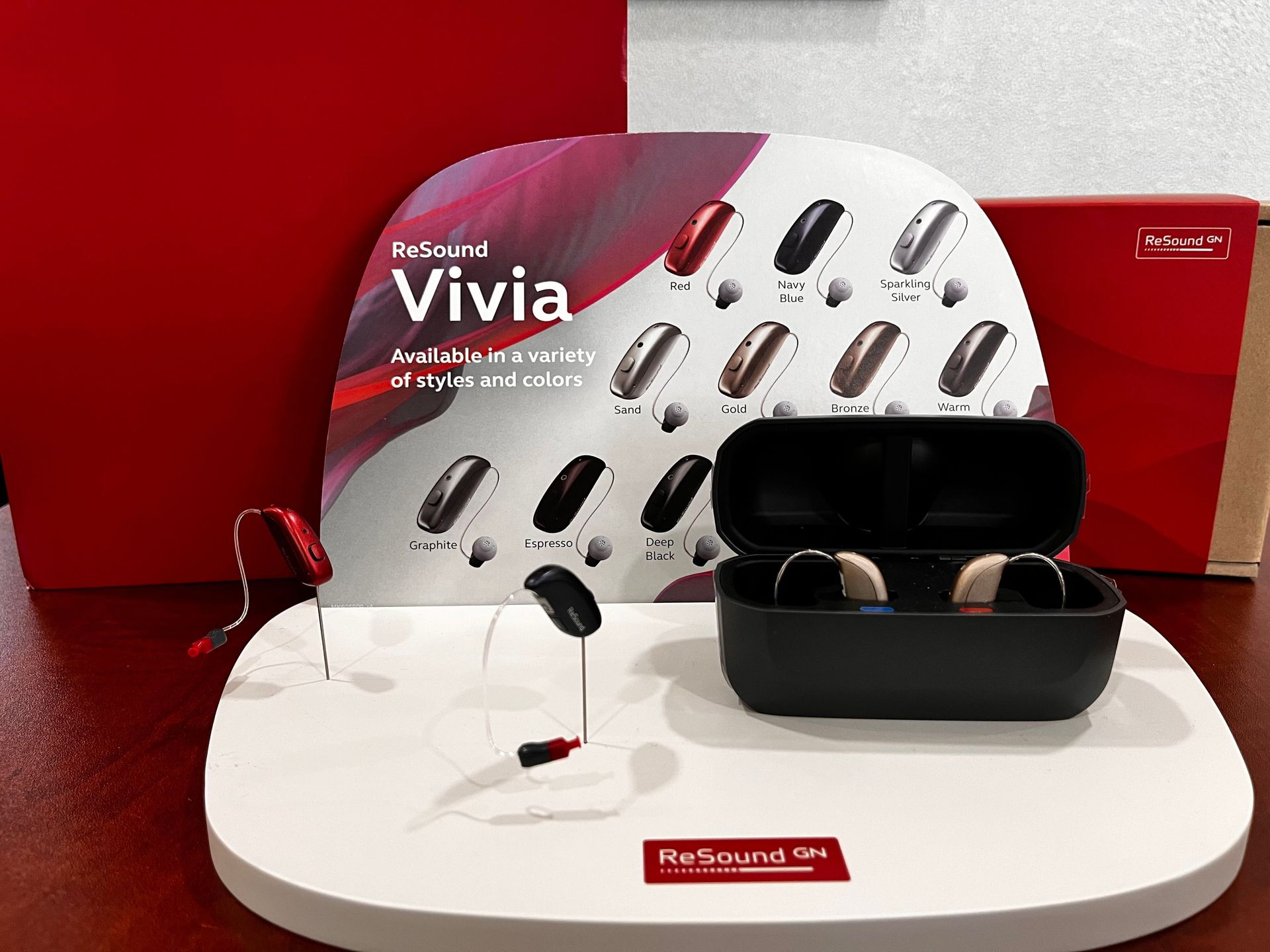 Items related to hearing aids on a red surface. Includes bags, a charger, and hearing aids.