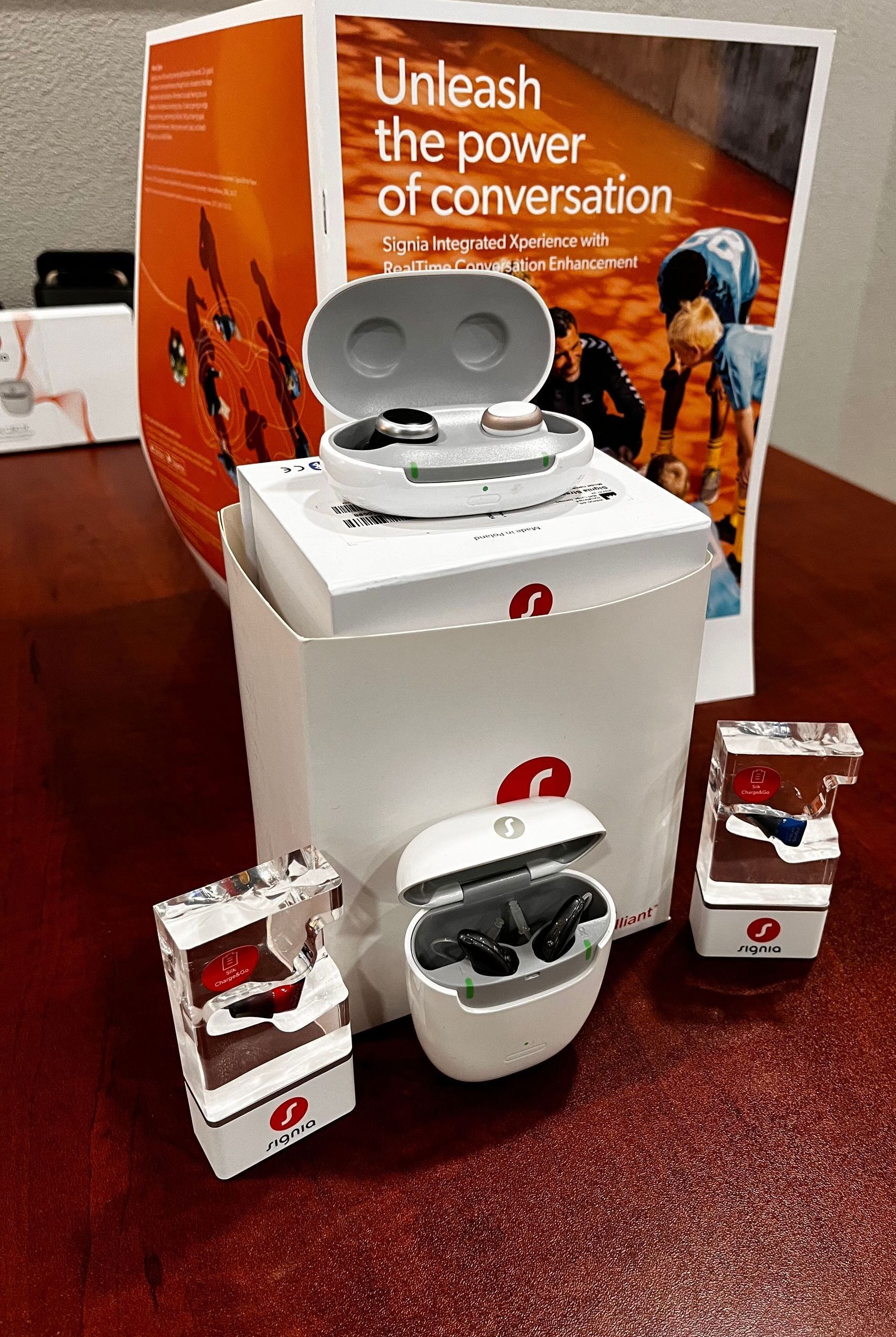 Items related to hearing aids on a red surface. Includes bags, a charger, and hearing aids.