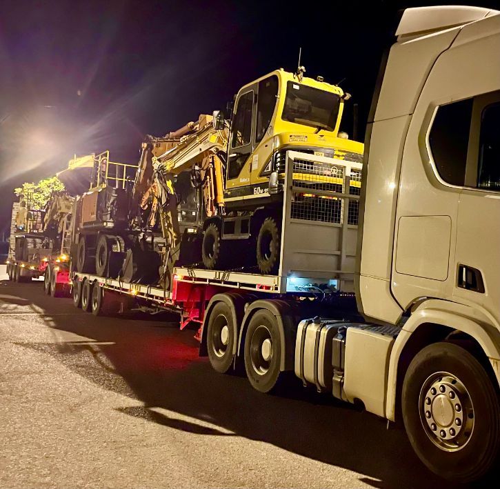 A White Semi Truck is Carrying a Load of Heavy Machinery on a Trailer — Goulburn Transport In Goulburn, NSW