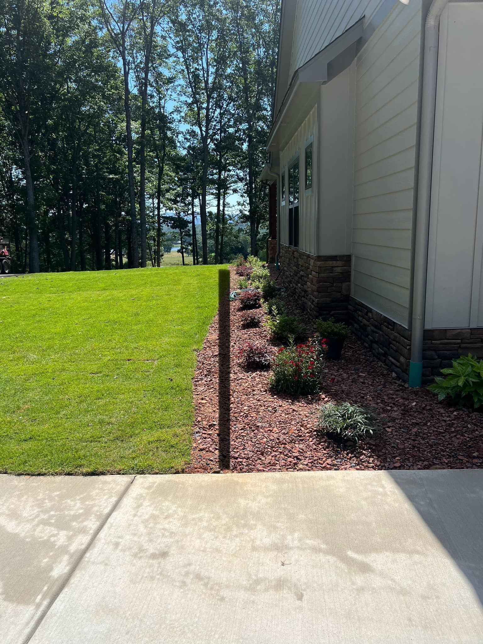 House exterior with a concrete driveway, red mulch landscaping, and a green lawn beside trees.