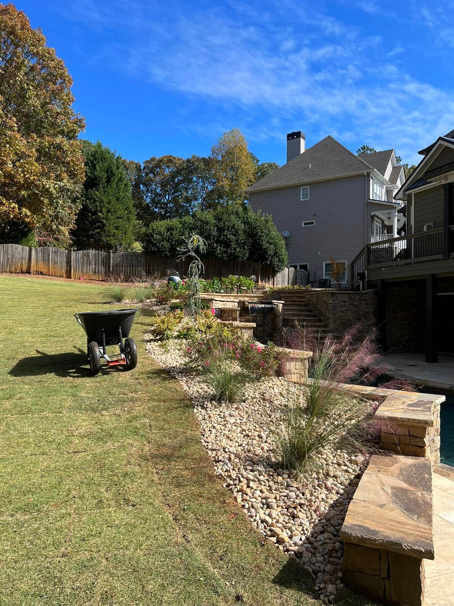 Sunlit backyard with lawn, flower beds, a black chair, and a patio beside a house.