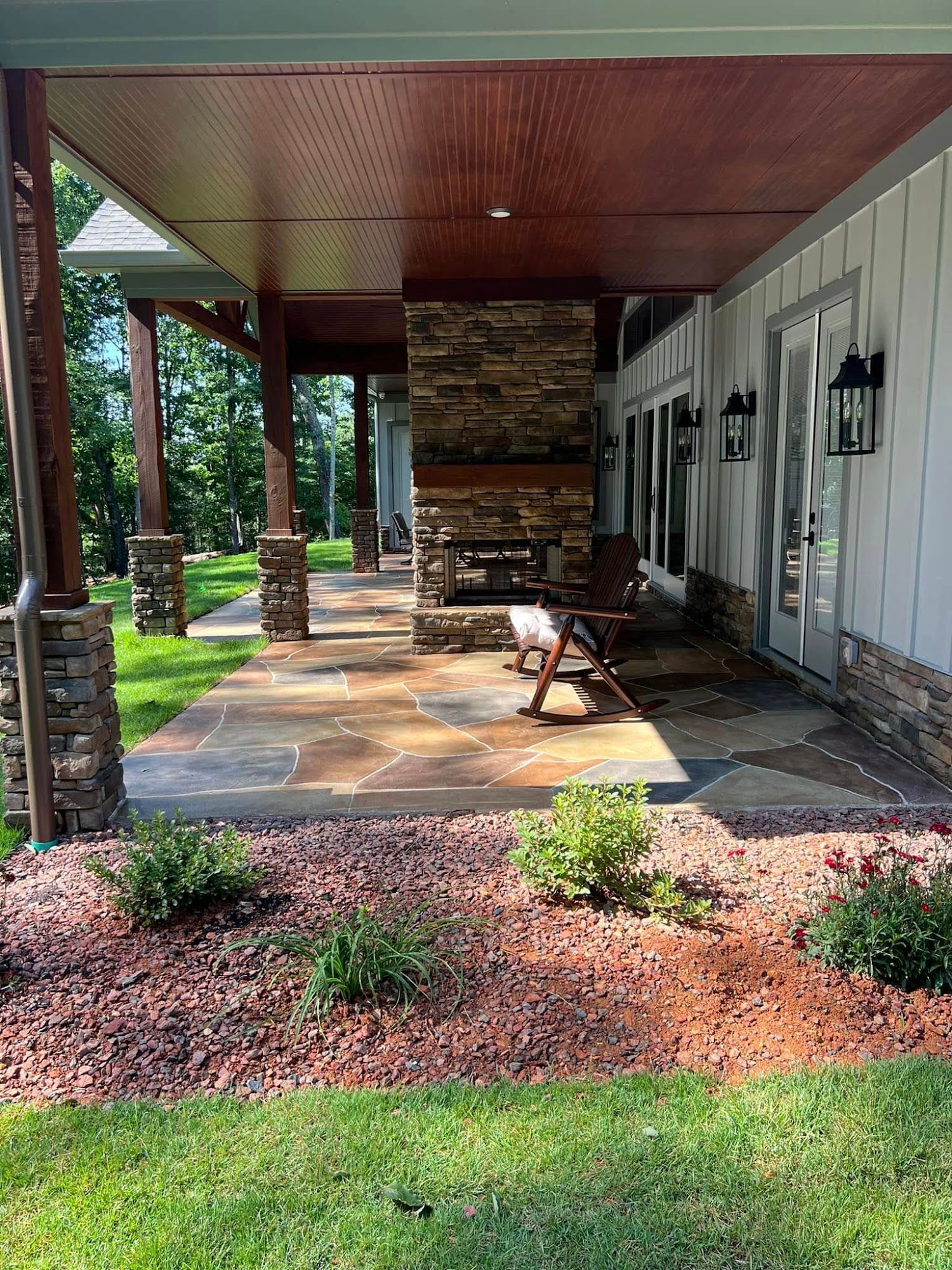 Covered front porch with stone column, bench, and lanterns beside a landscaped lawn.