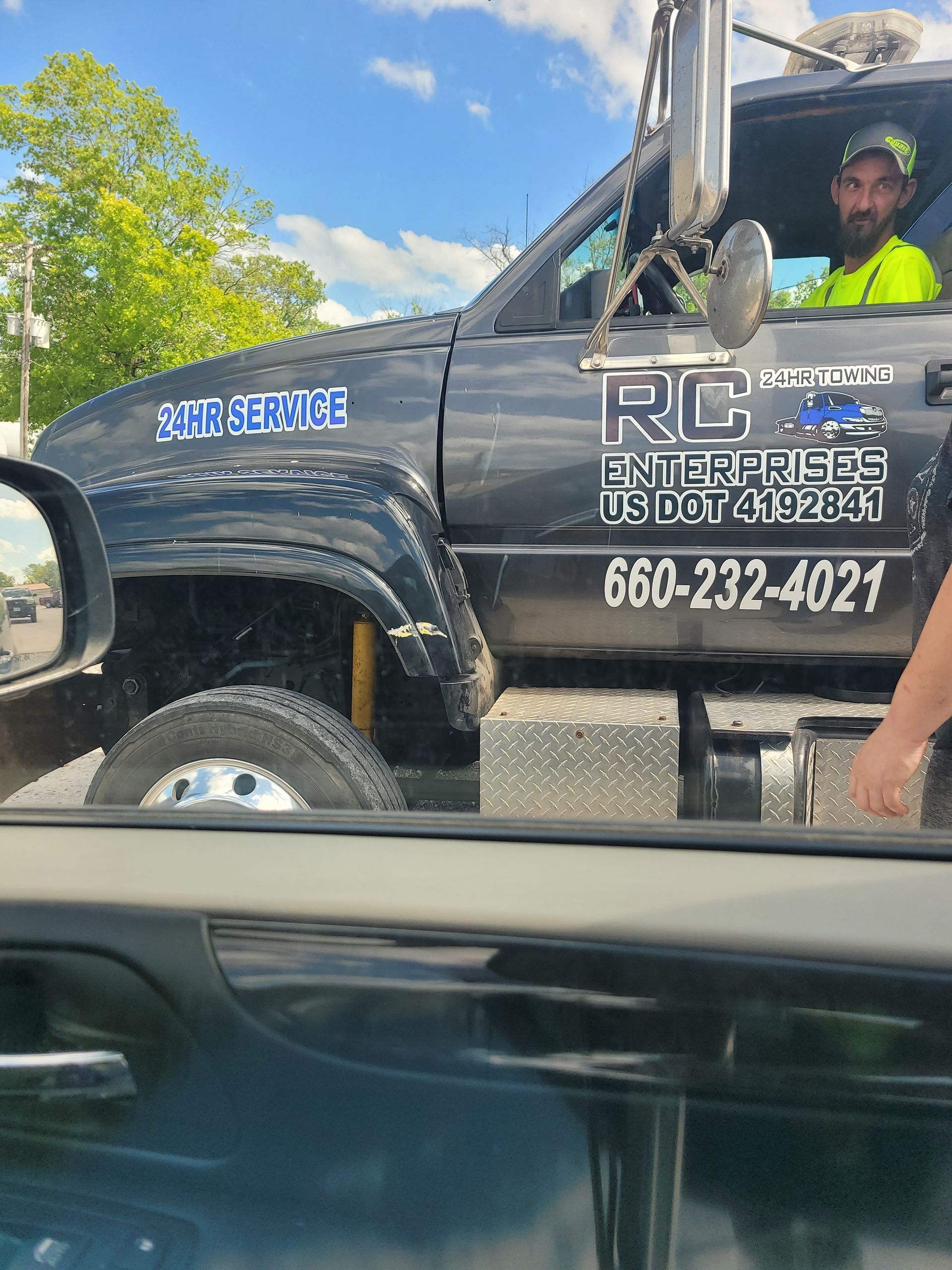 Tow truck with driver, black truck, blue lettering, yellow safety vest, road.