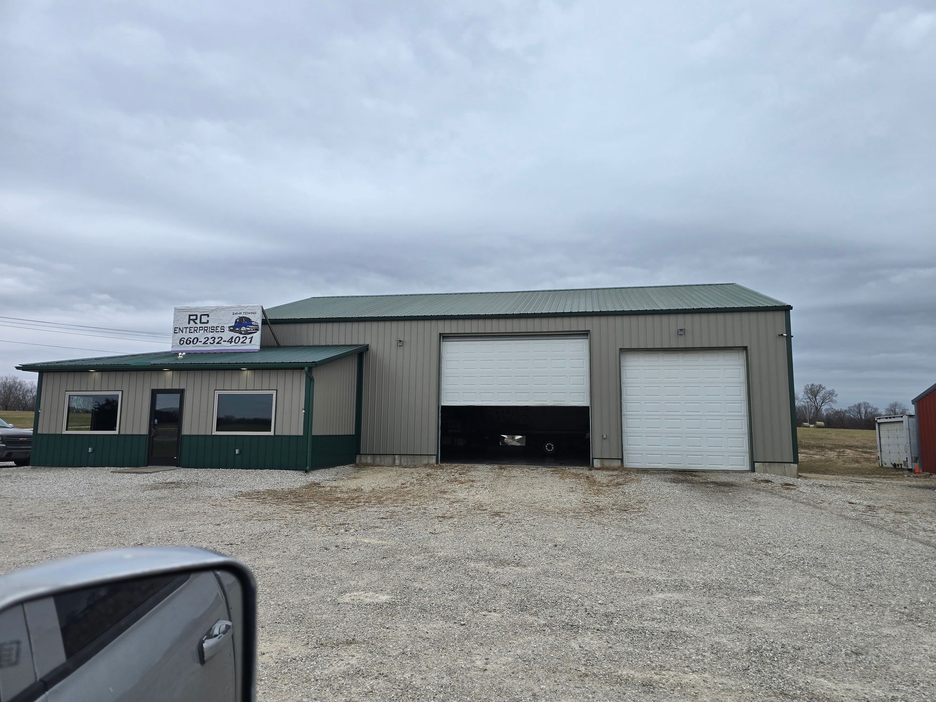 A gray metal building with garage doors and a small office. Sign says 