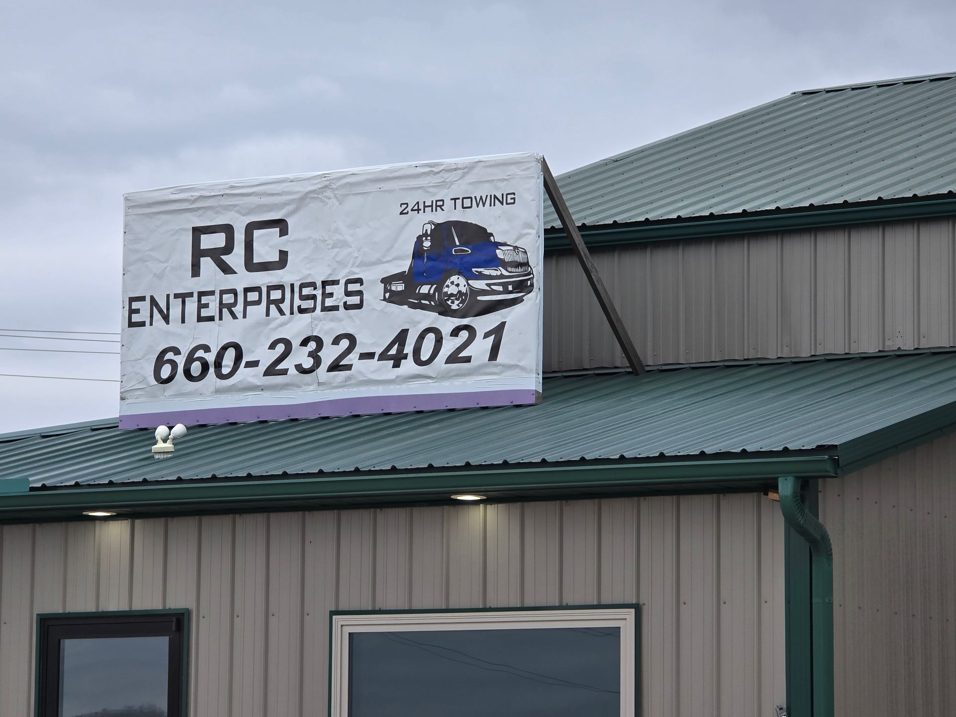 Sign for RC Enterprises with truck graphic and phone number; gray building and cloudy sky.