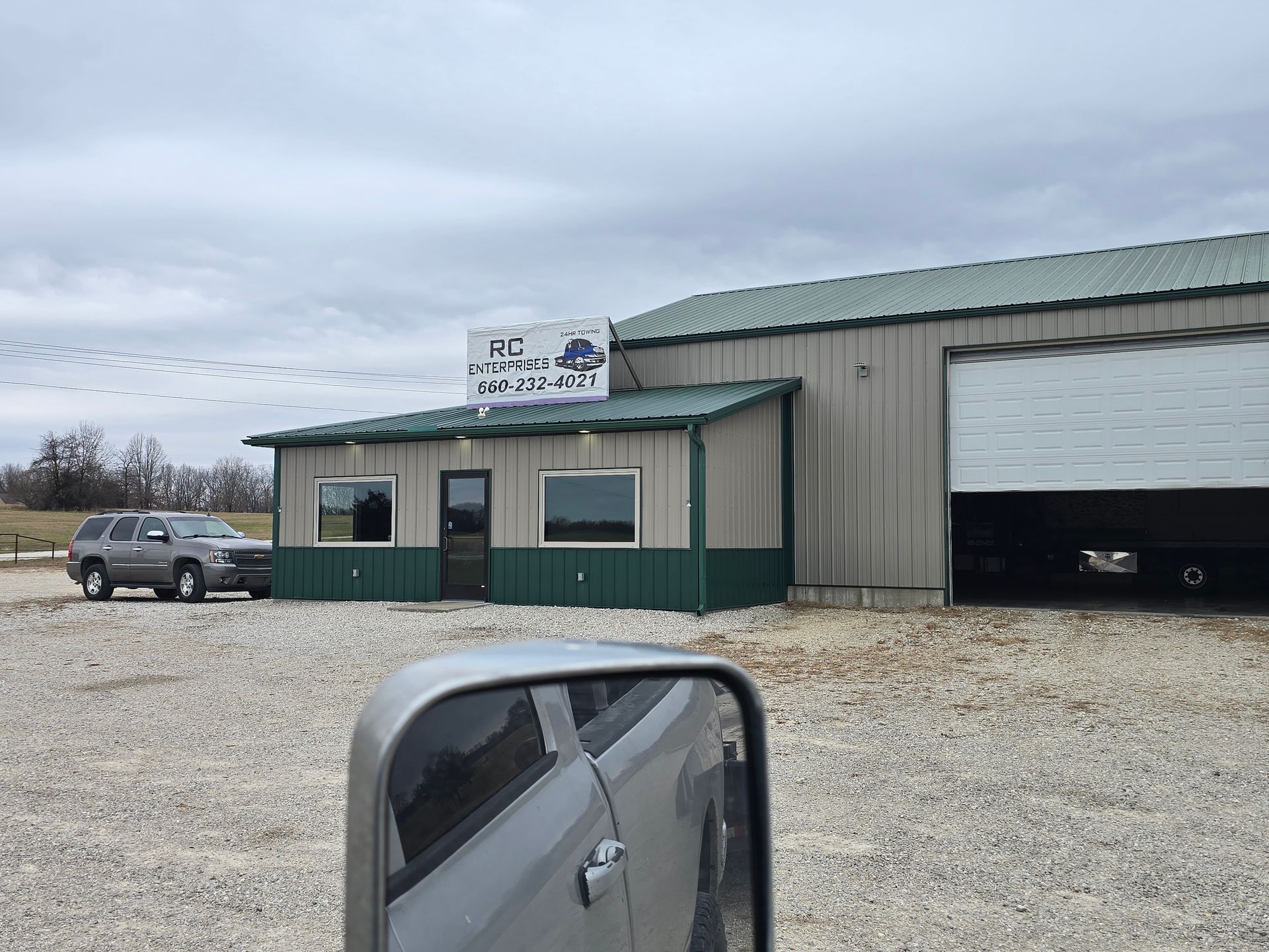 A gray building with a sign, a parked SUV, and a garage door open; overcast sky.