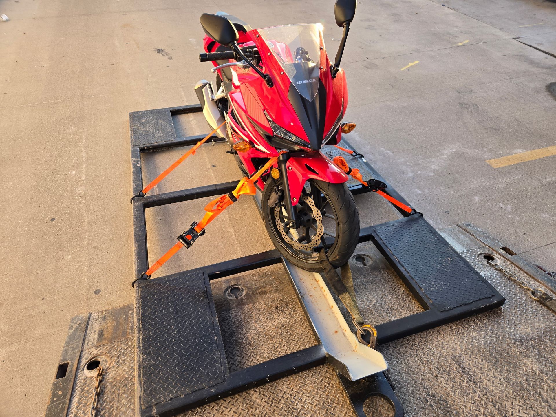 Red motorcycle secured on a black flatbed tow truck, ready for transport.