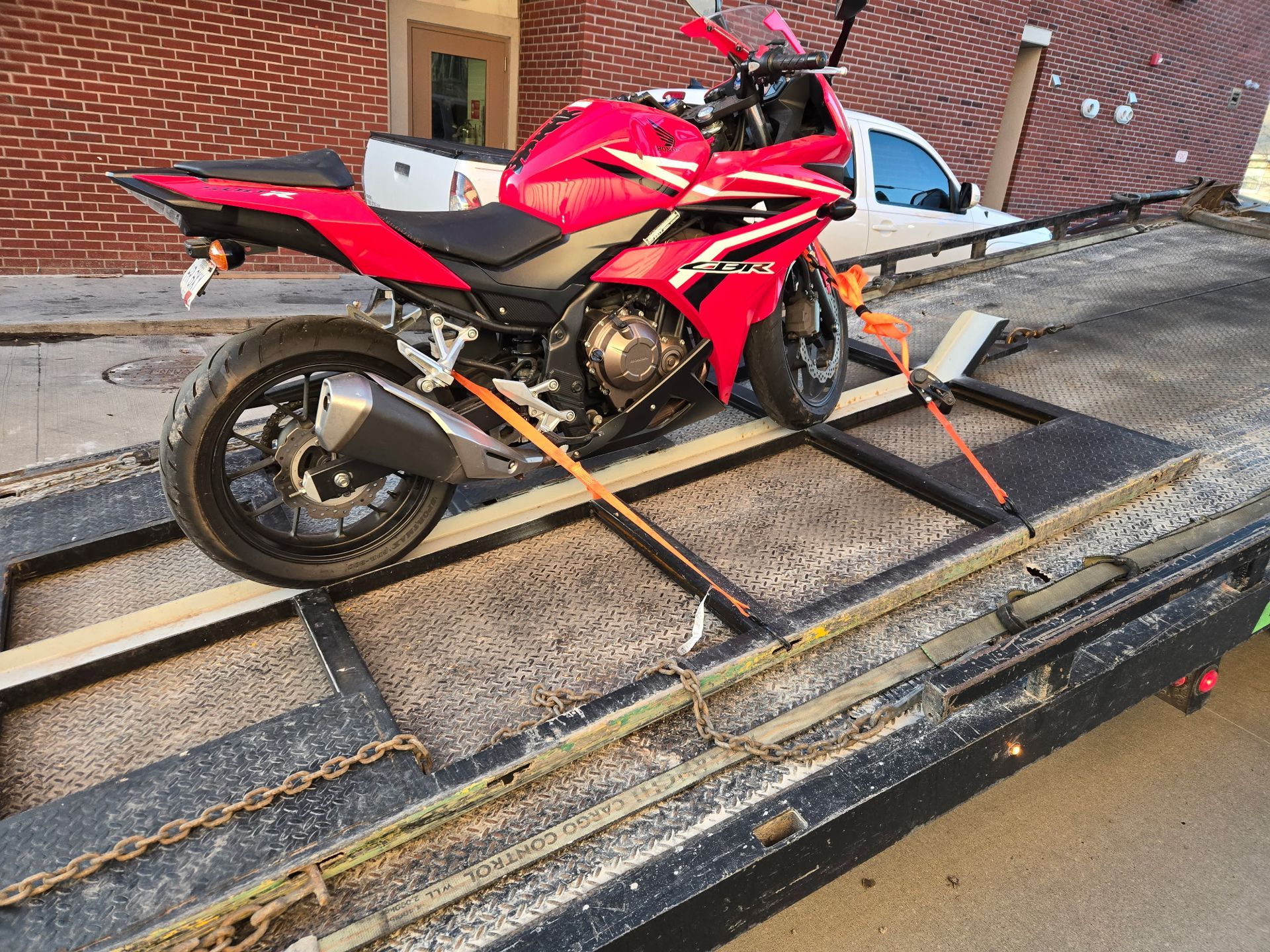 Red Honda motorcycle strapped to a tow truck bed.