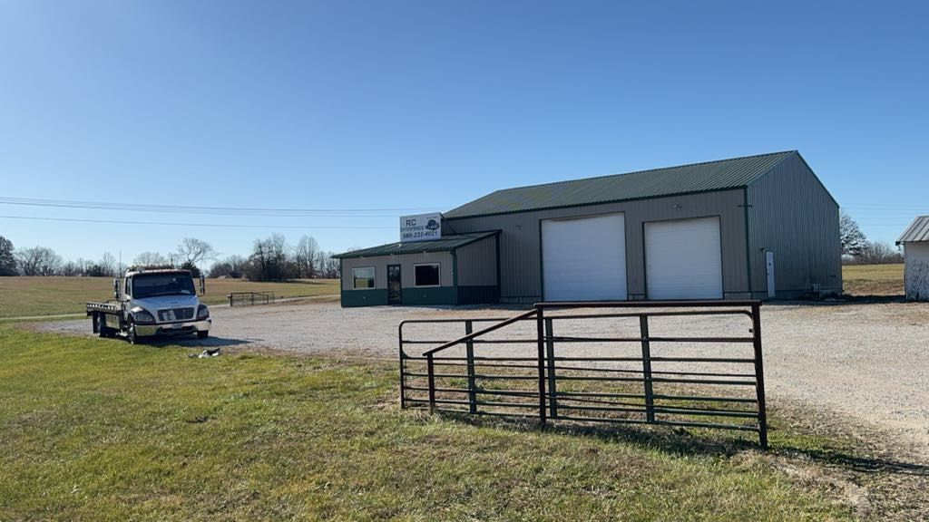 A truck parked in front of a tan building with green roof and two garage doors, under a blue sky.