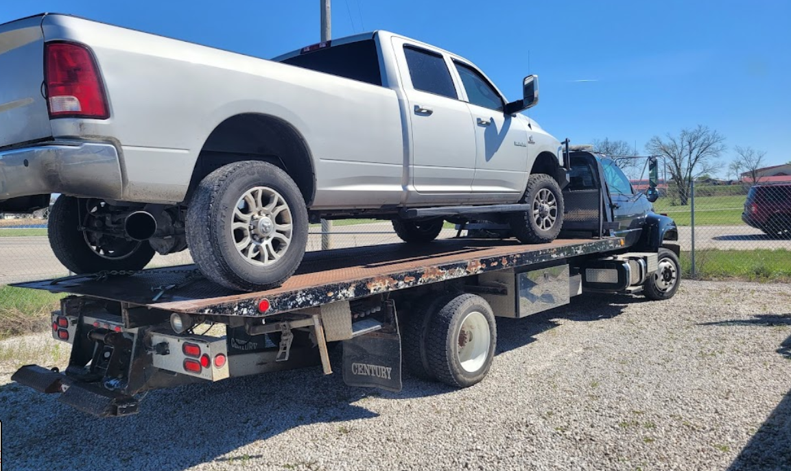 Silver pickup truck on a black flatbed tow truck on a sunny day.