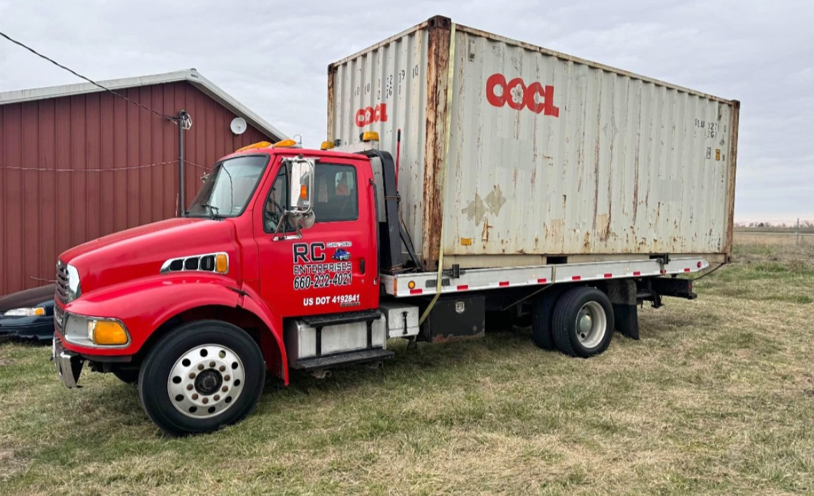 Red Sterling truck with shipping container, parked on grass. Container has 