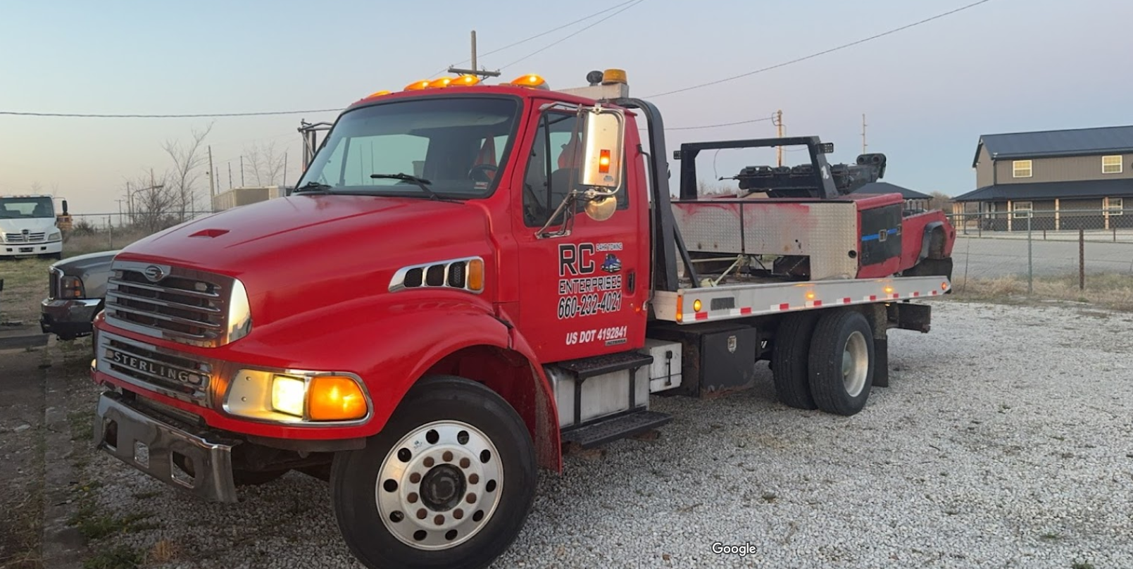 Red tow truck parked in front of a building with the sun setting.