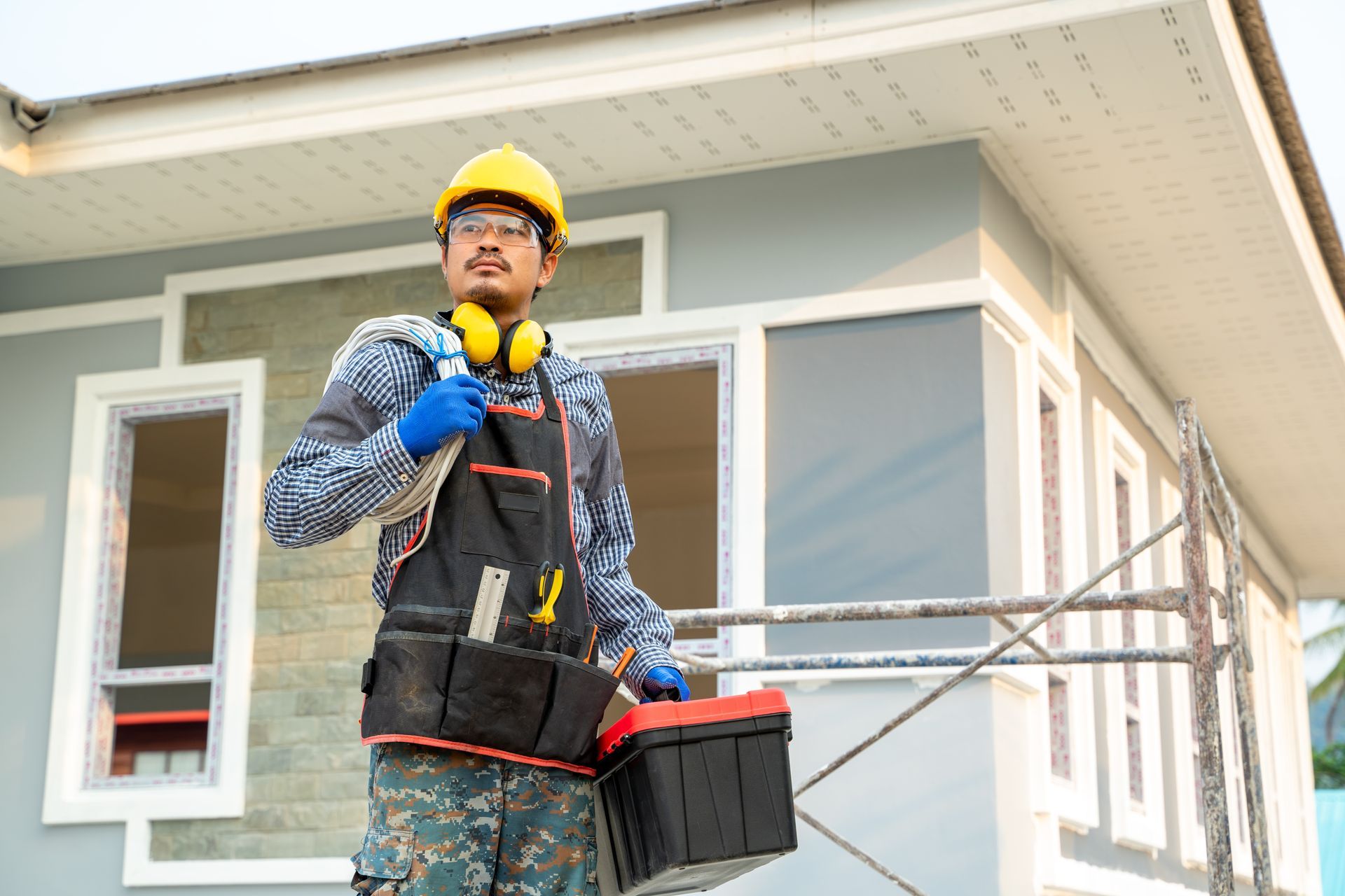 A man is standing in front of a house holding a toolbox.