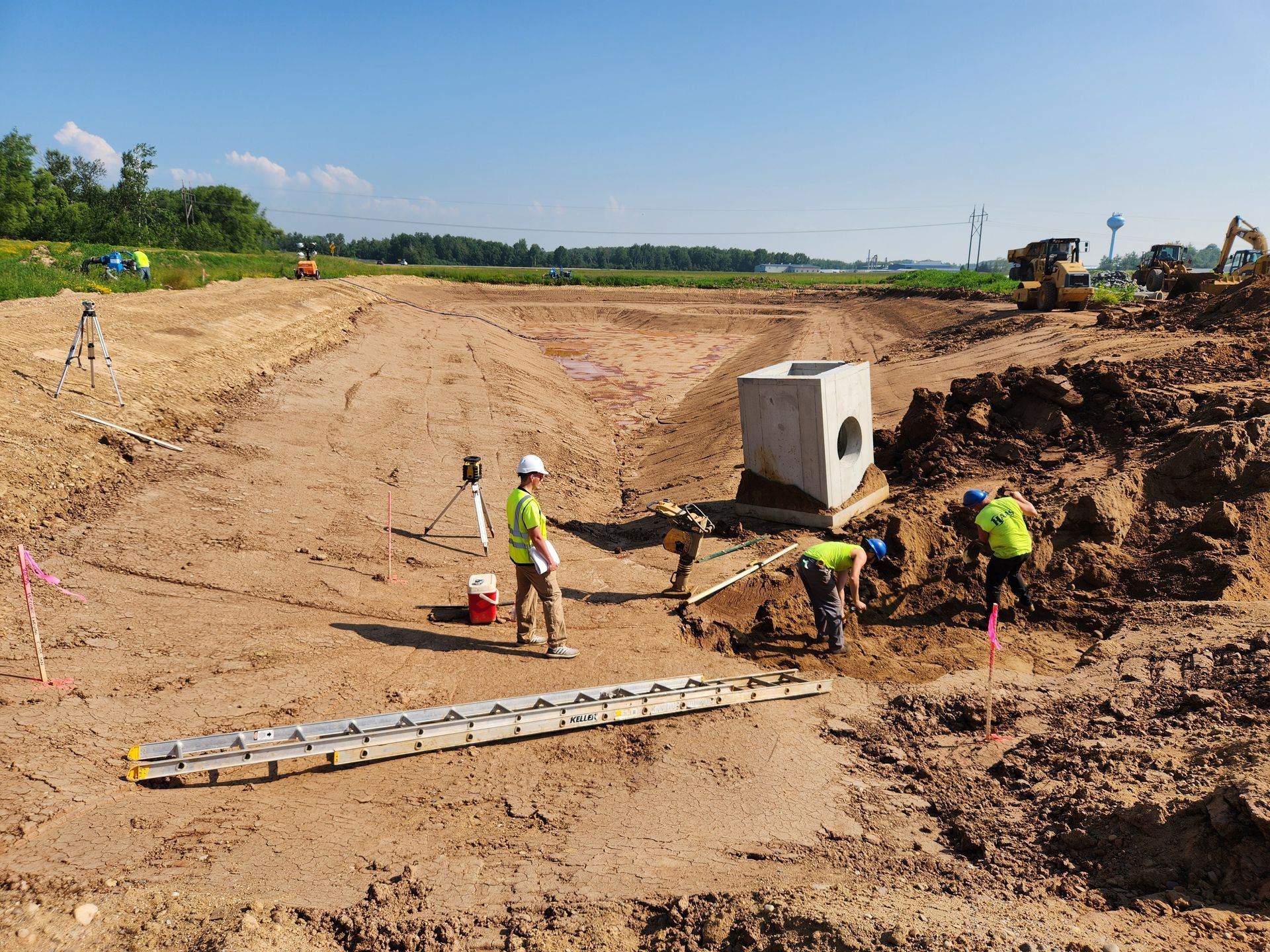 Construction workers surveying and excavating at a construction site, near a concrete structure, on a sunny day.