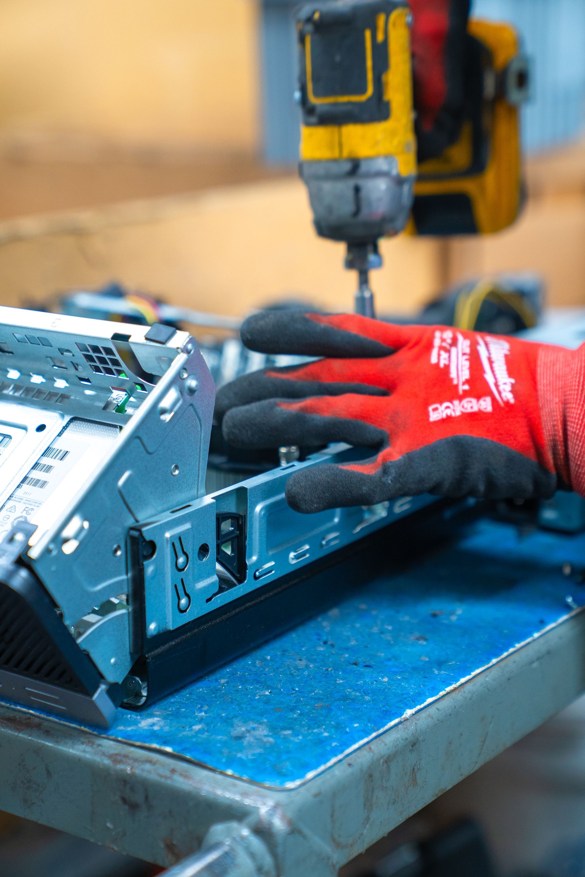 A person wearing red gloves is using a drill on a piece of metal.