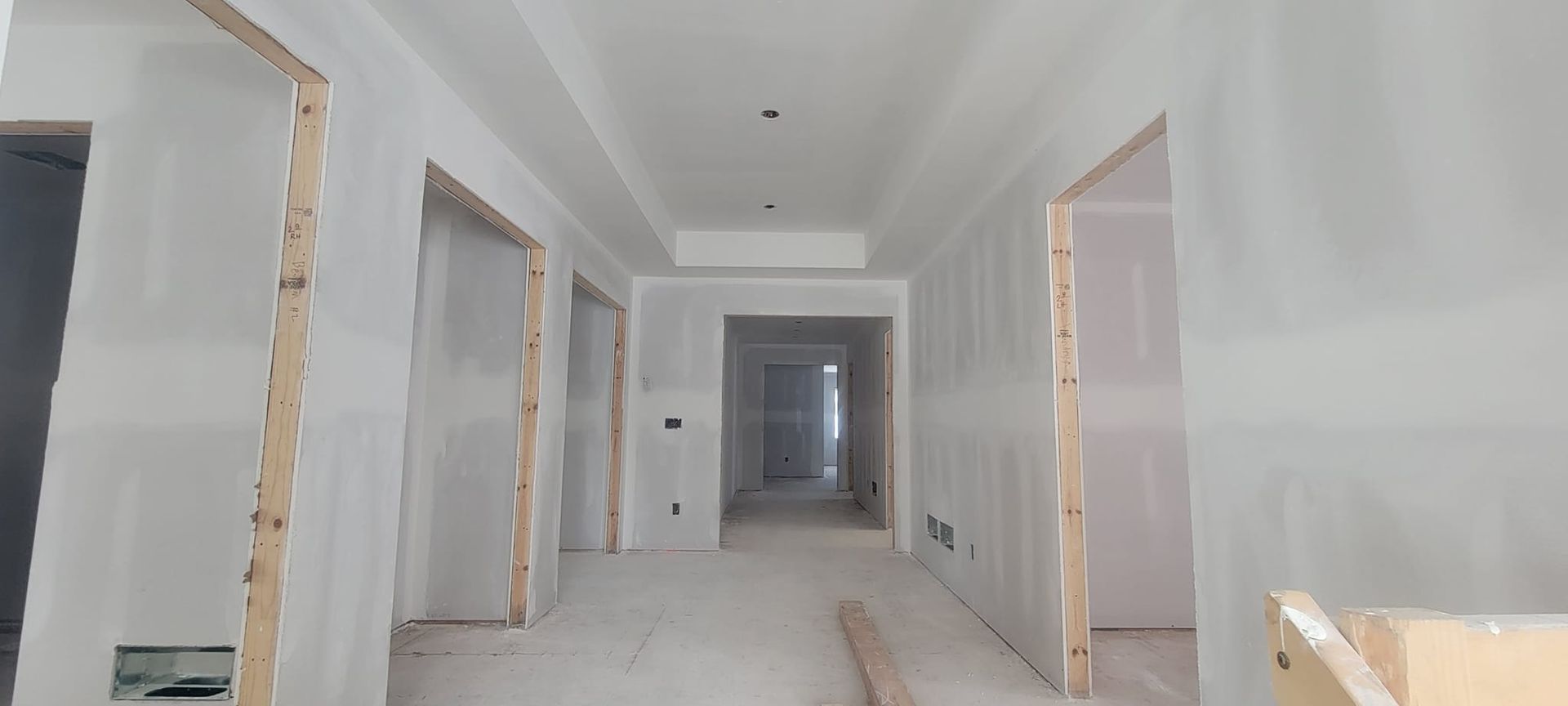 Hallway under construction, unfinished walls with drywall and wooden door frames.