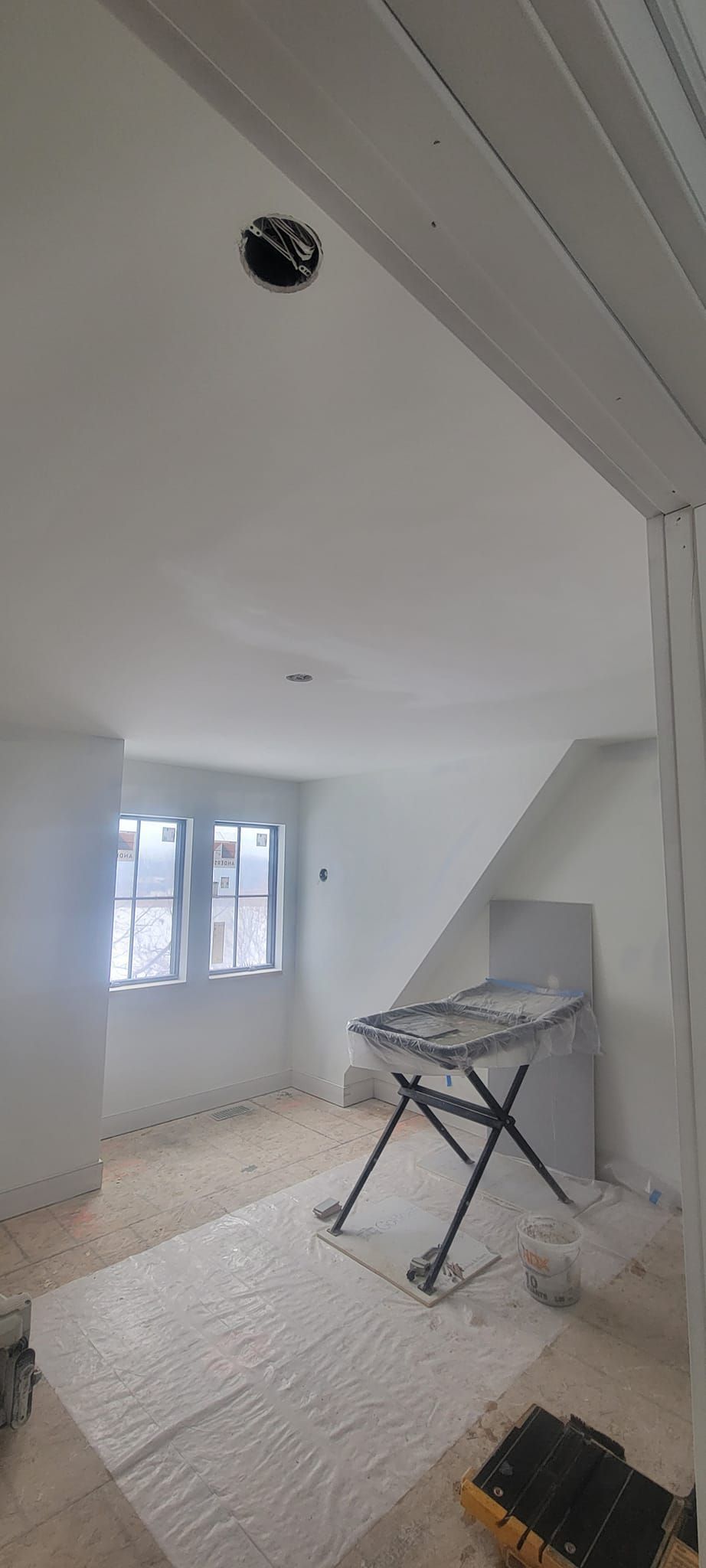 Interior room, freshly painted white. A folding table and stairs are visible.  A window provides natural light.