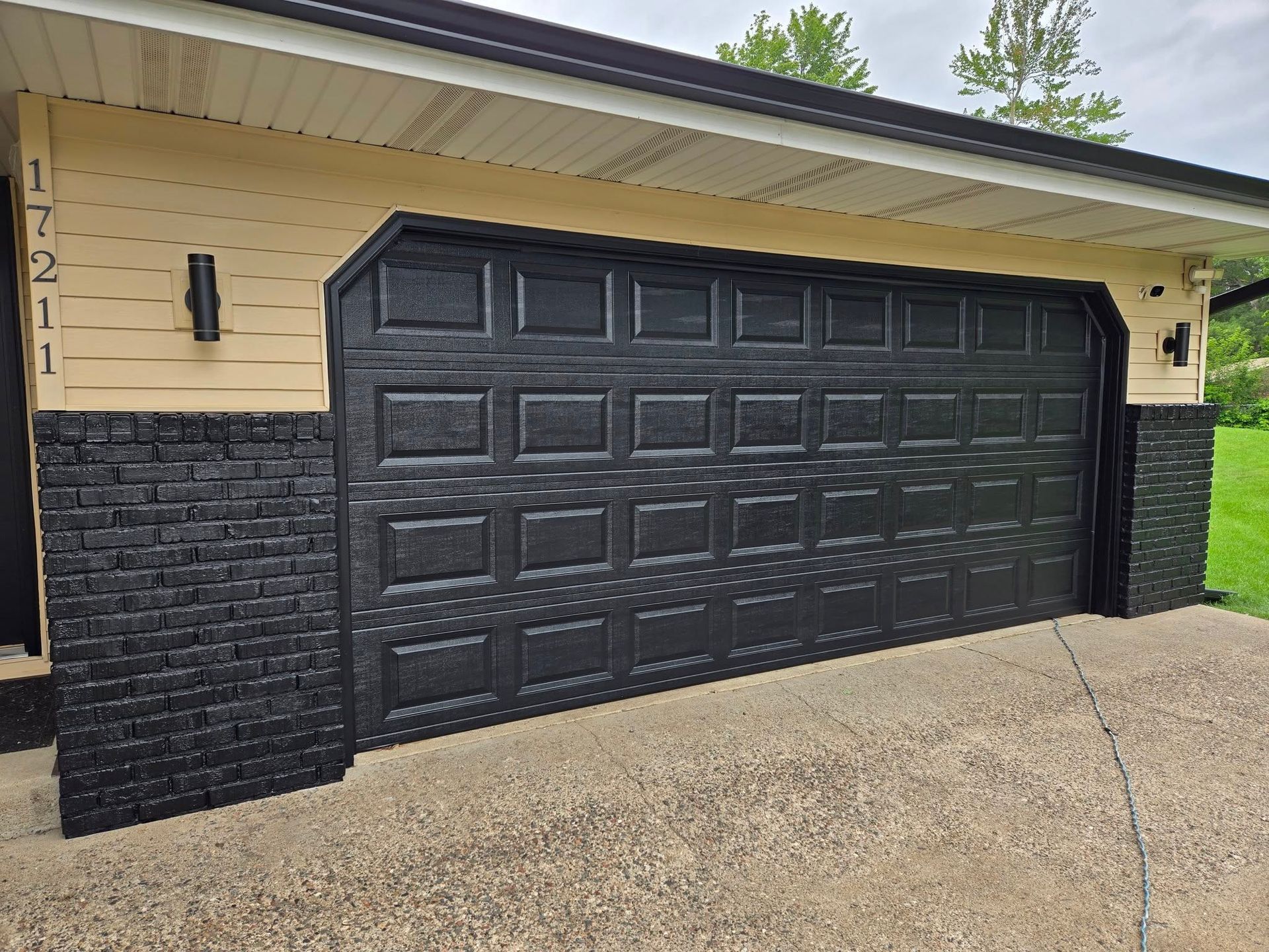 Black garage door with black brick facade, tan siding, and address 