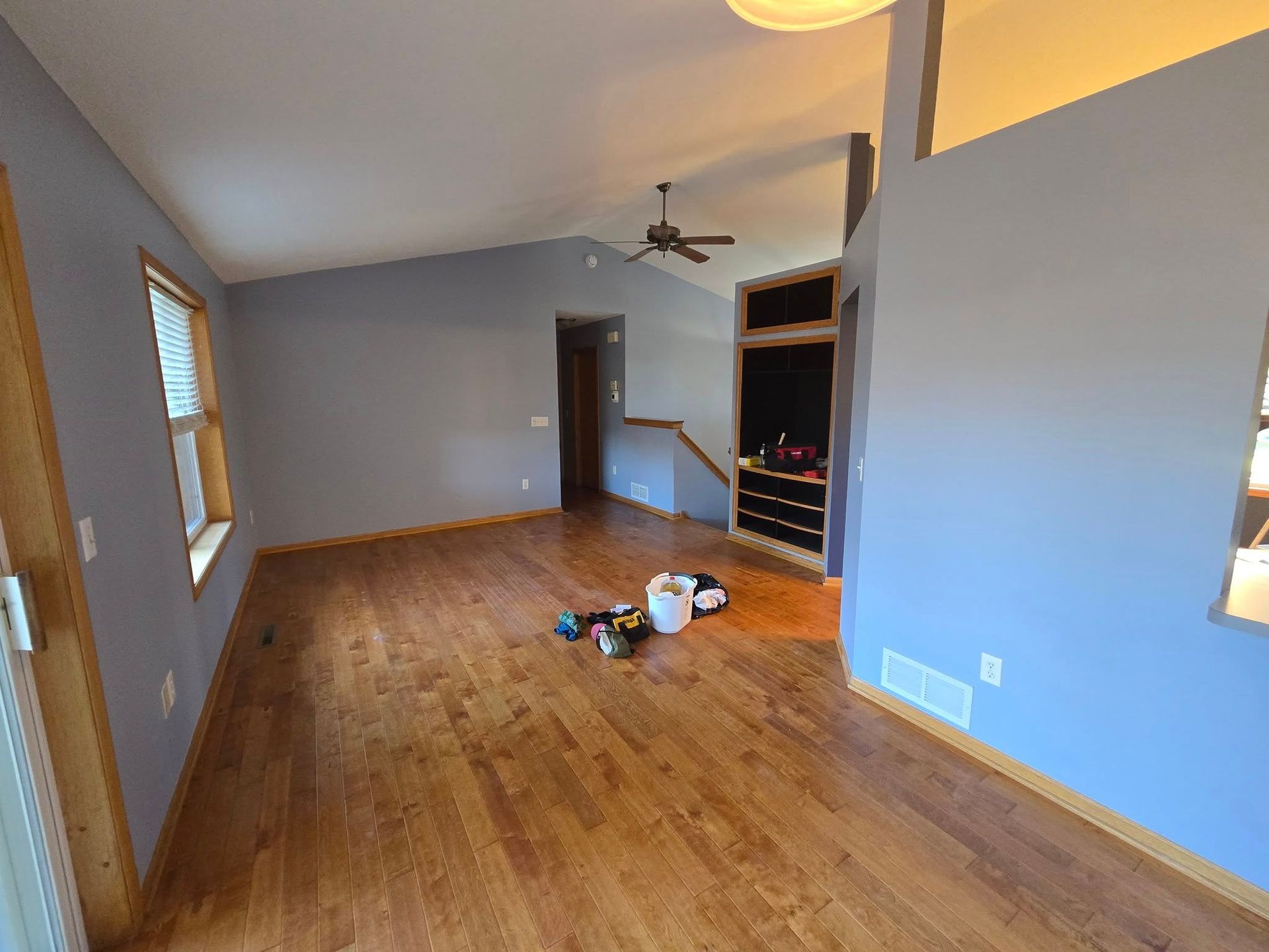 Empty living room with wood floor, blue walls, a ceiling fan, and some tools on the floor.