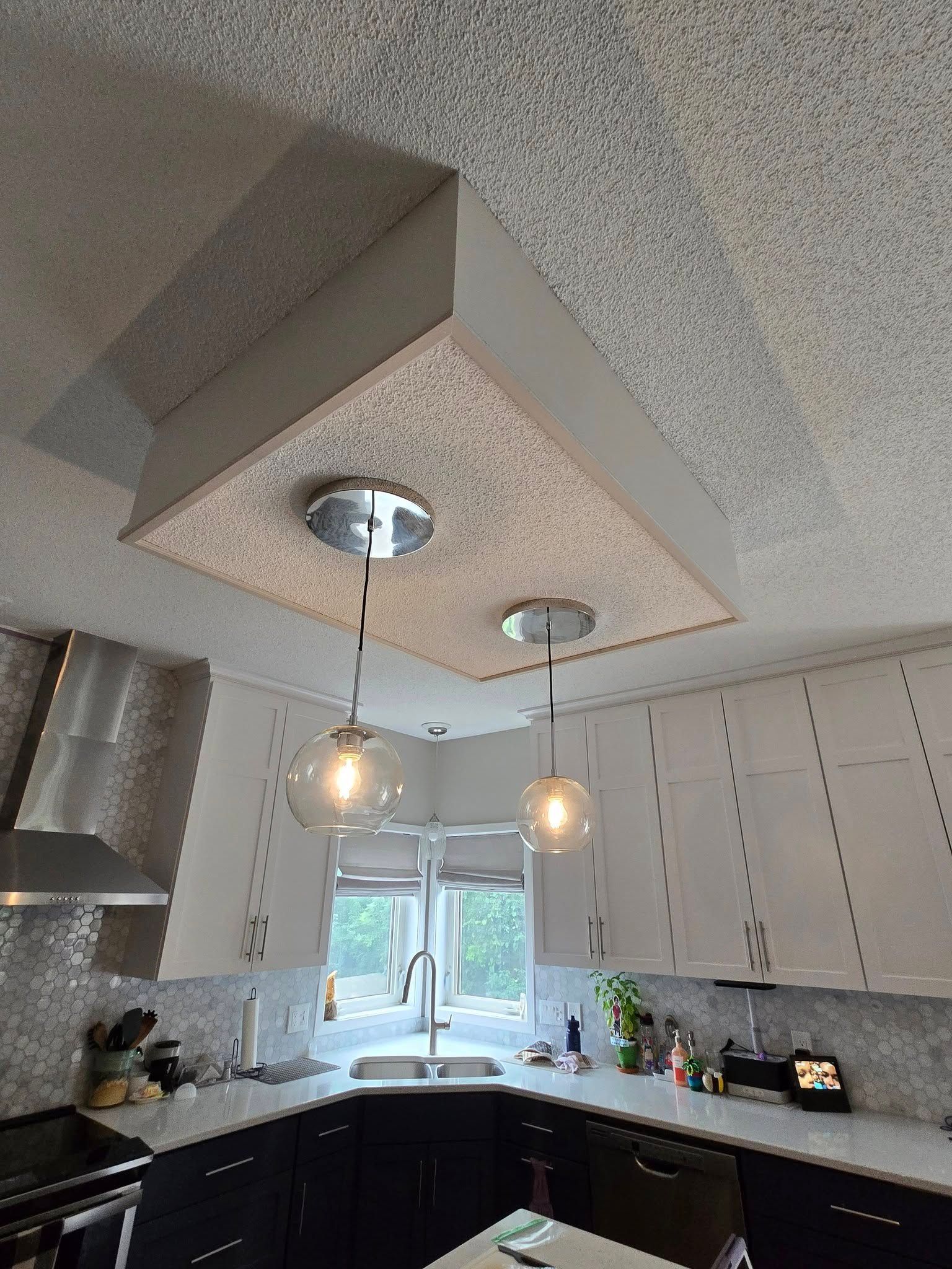 Kitchen with black and white cabinets, range hood, and pendant lights hanging from a textured ceiling panel.