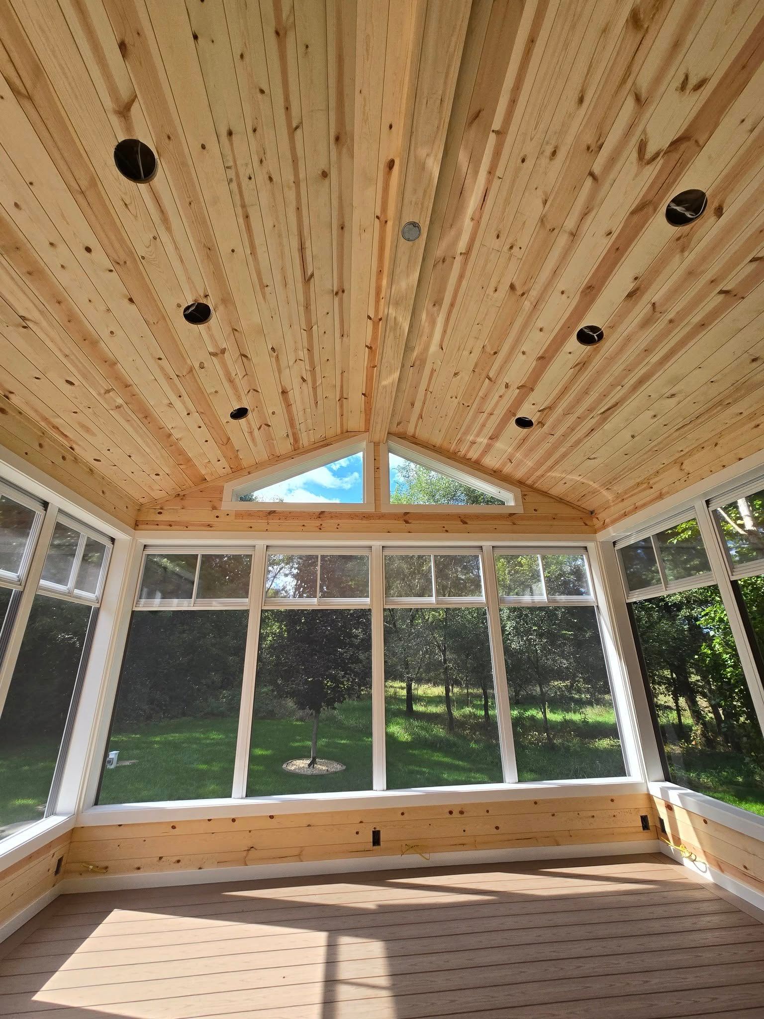 Sunroom interior with wood ceiling, windows, and a view of green trees.