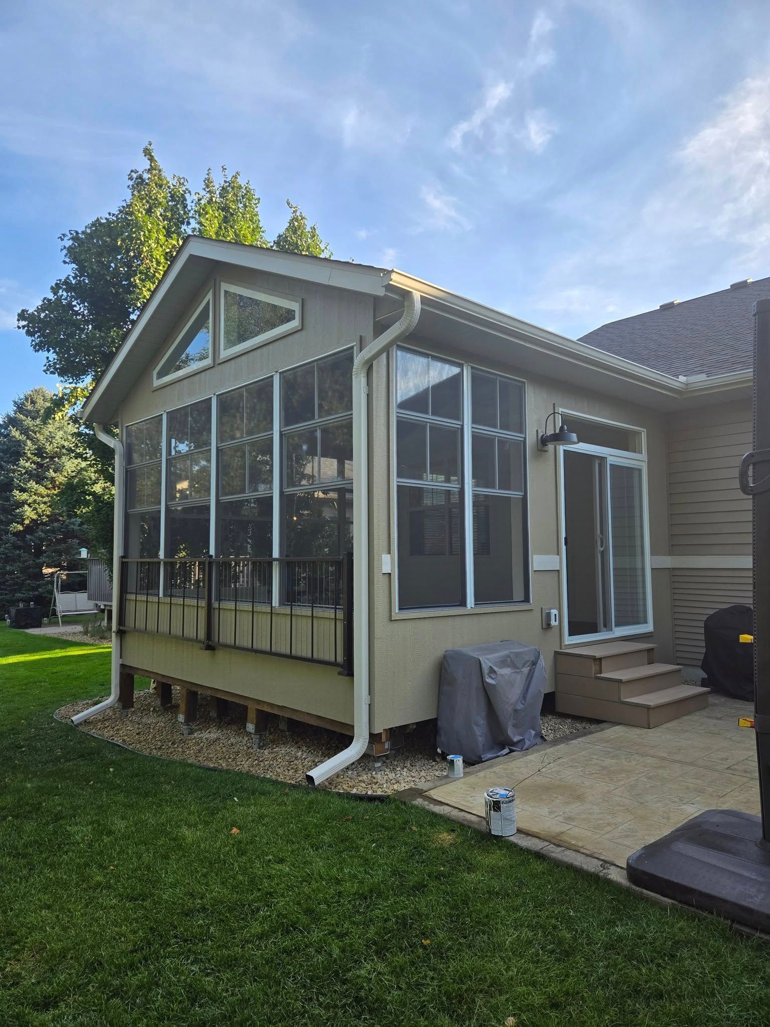Screened-in porch attached to a house with glass windows and a door, set in a grassy yard.