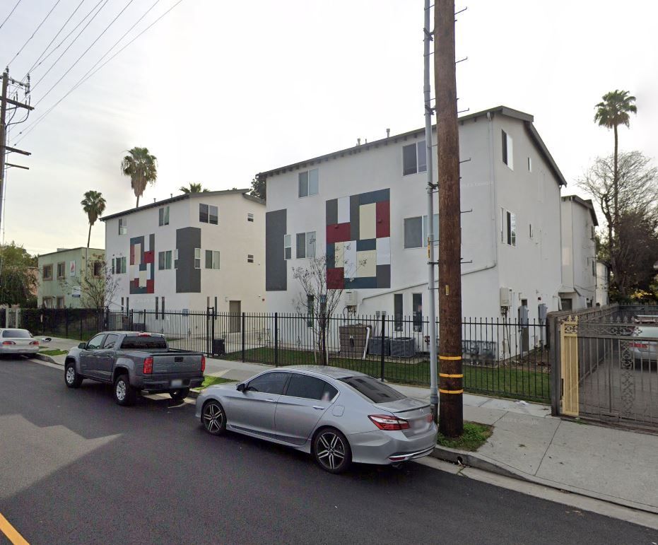 A silver car is parked on the side of the road in front of a white building