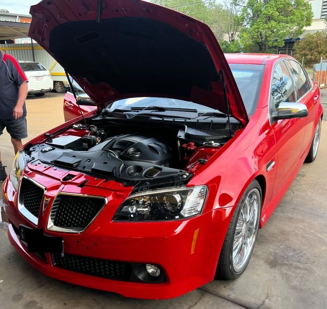 Red car with hood open, showing engine. Chrome grill and wheels; person nearby— Bundaberg Radiator Service in Bundaberg East, QLD