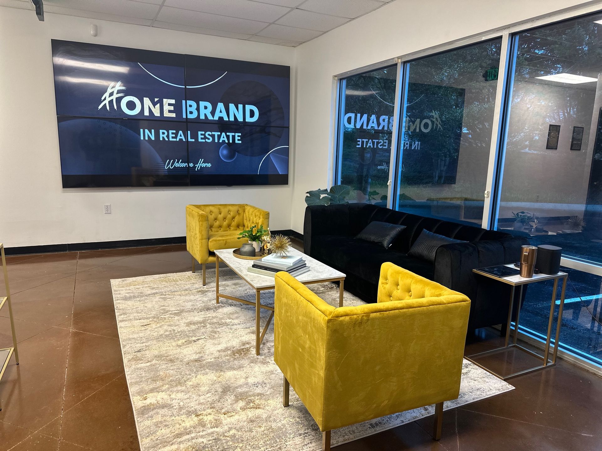 A living room with a couch , chairs , coffee table and a sign that says one brand in real estate.