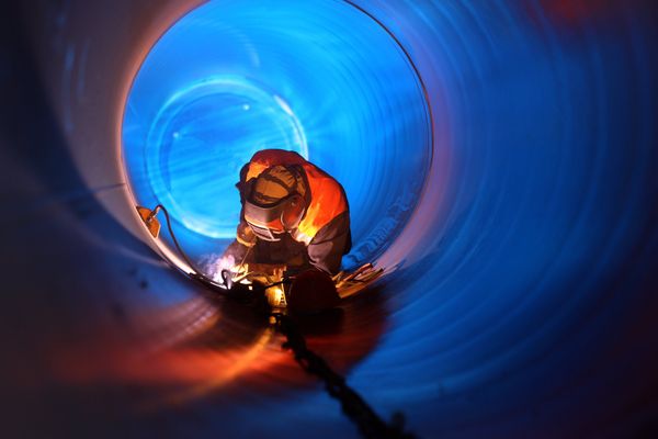 A welder from Sylvan Lake Welding works inside a metal pipe.