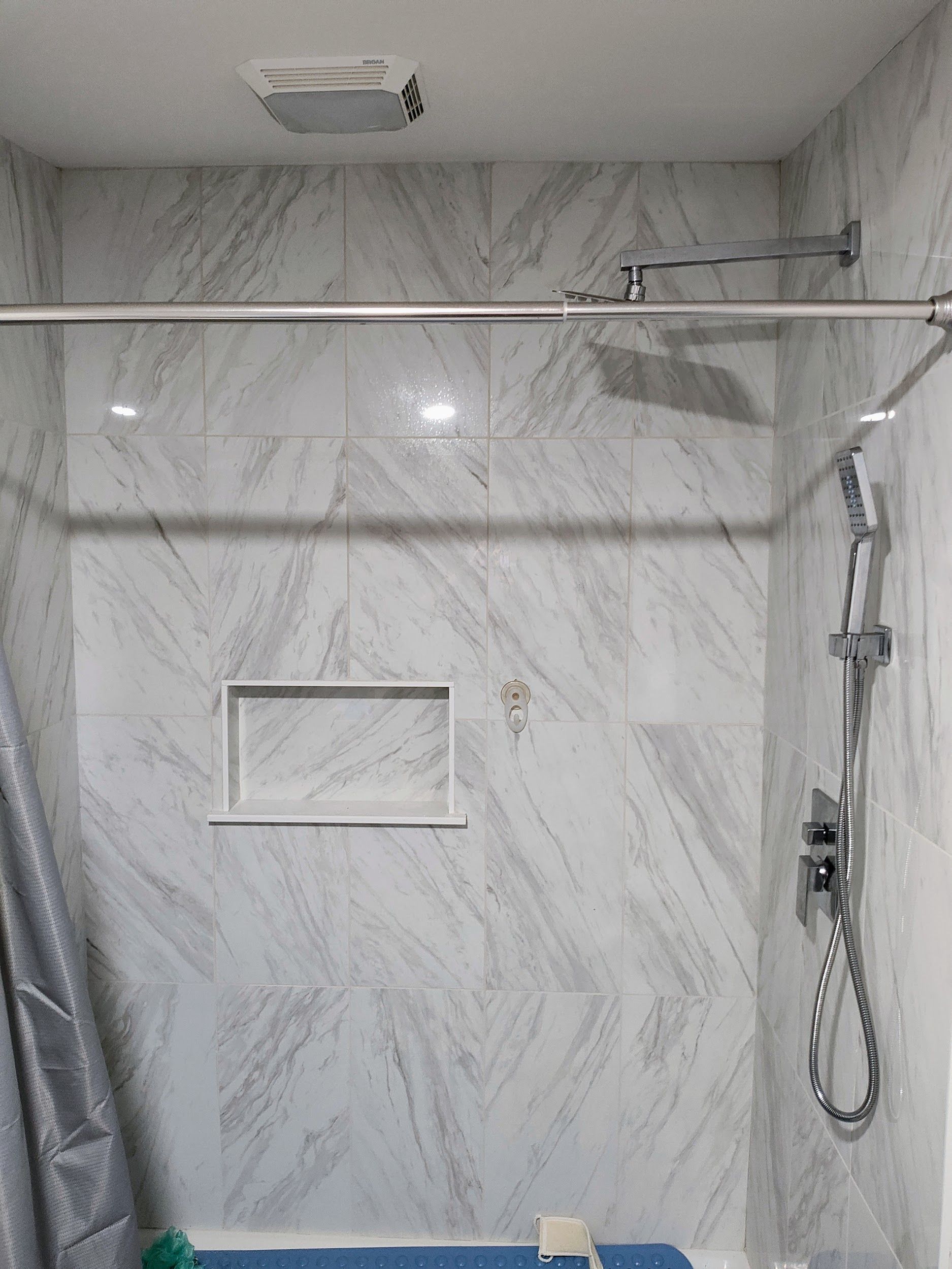 Shower with white marble-look tile, showerhead, and glass enclosure.