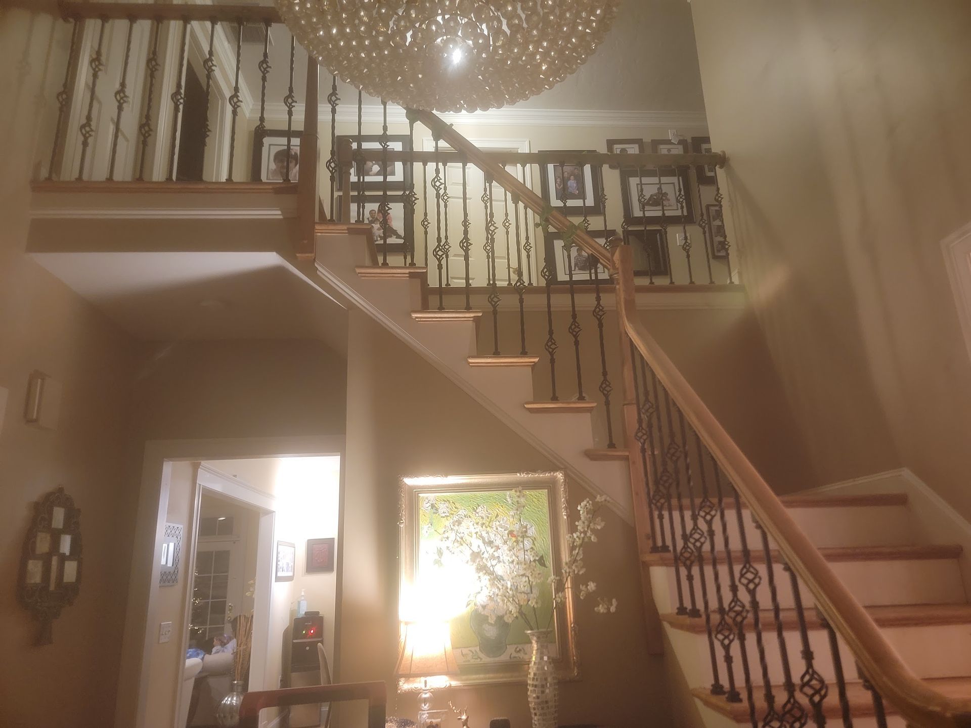 Interior view of a grand staircase with decorative black iron railings and a large chandelier.