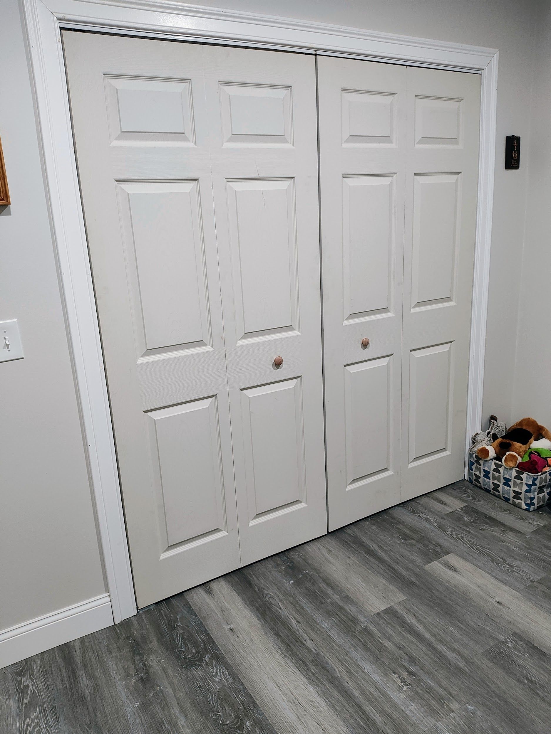 White bi-fold closet doors on a gray floor, with white trim. A basket with items is on the right.