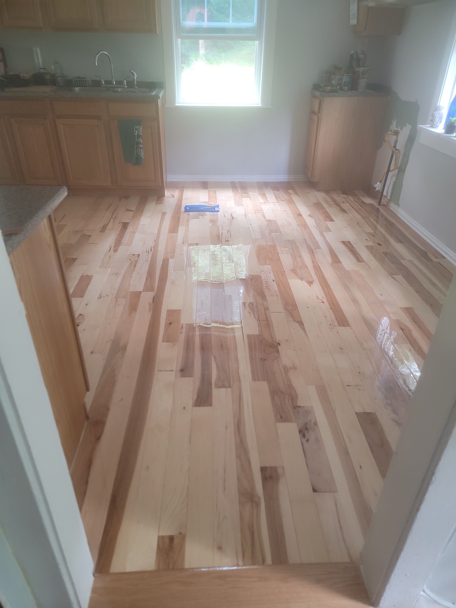 Newly installed hardwood floor in a kitchen with wooden cabinets and a window in the background.