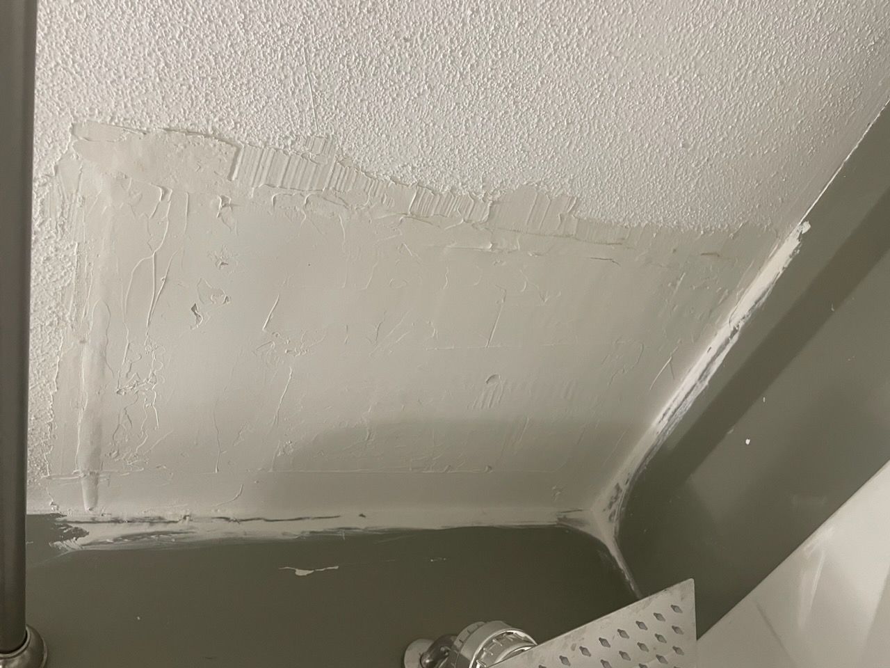 Ceiling repair with textured patch and gray wall corner; a silver tool is present.