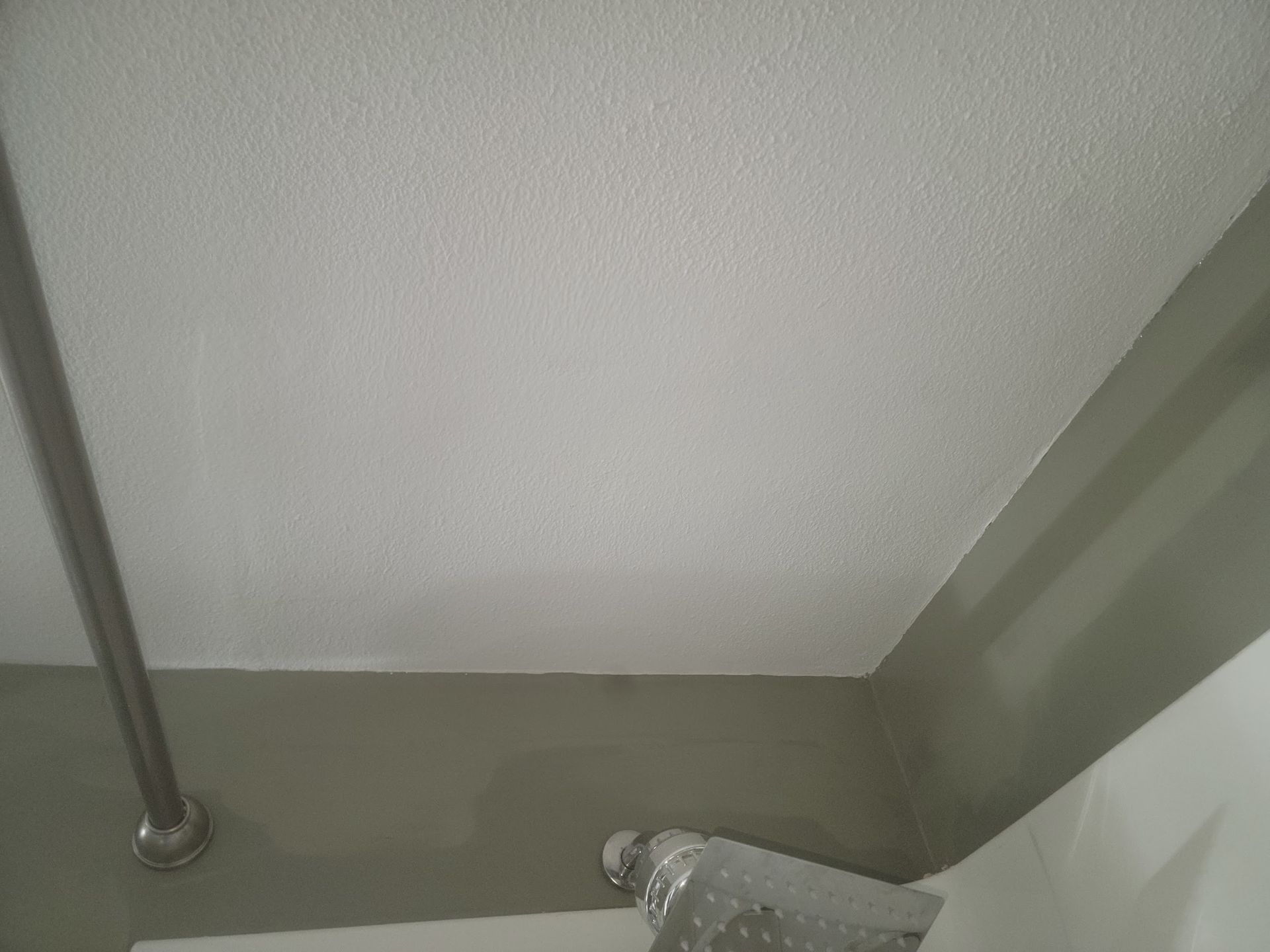 A white, textured ceiling meets a light gray wall, with a metal pole and ventilation visible.