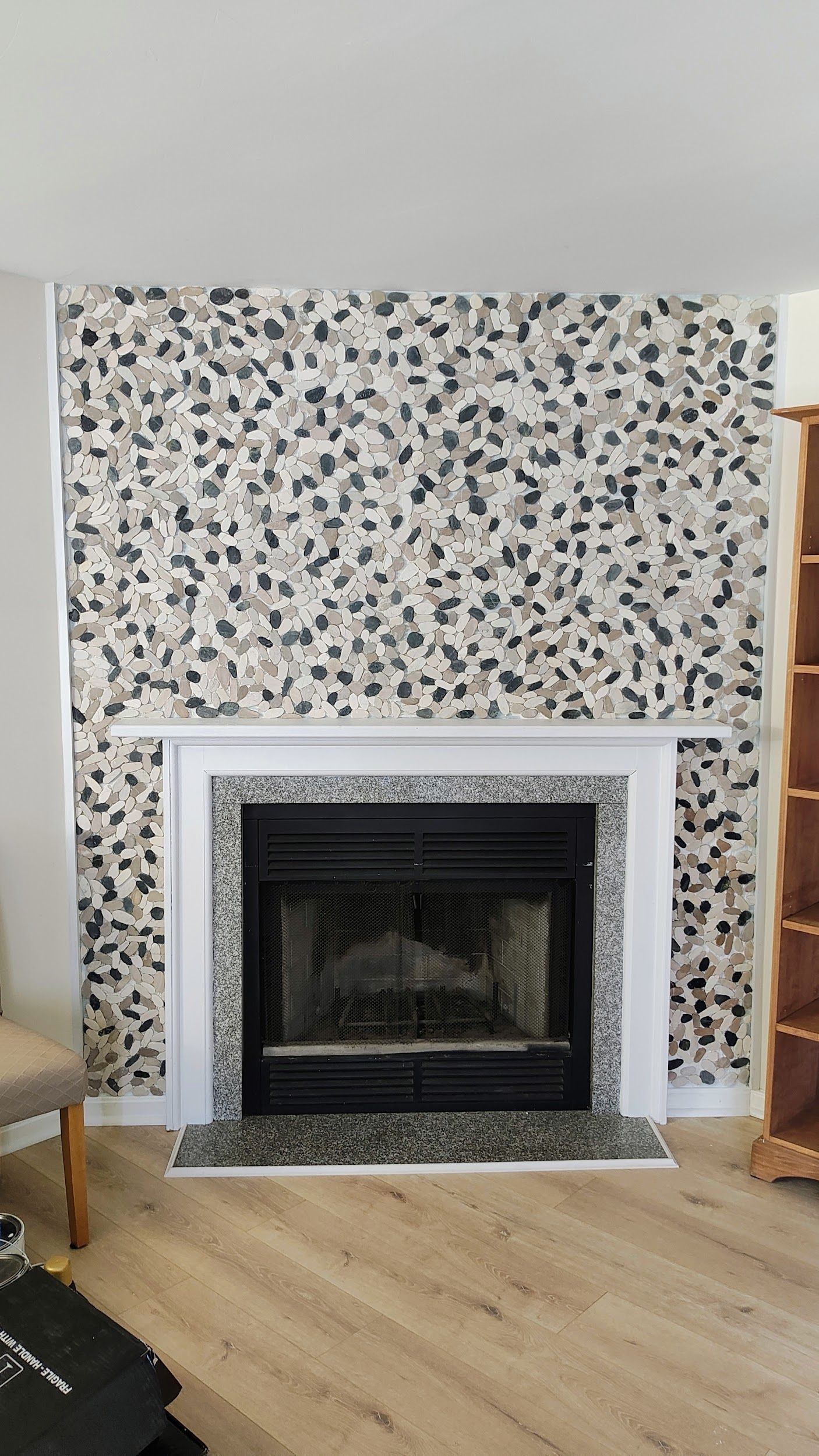 Fireplace with pebble-tiled wall and white mantel. Wooden floor and a bookshelf are visible.