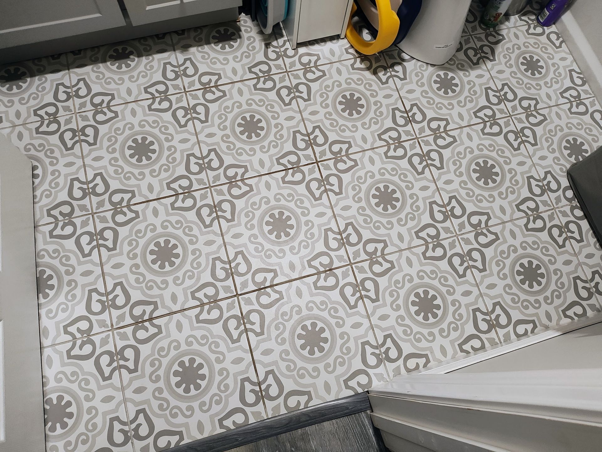 Gray and white patterned floor tiles in a room with a cabinet, a toilet, and part of a wall.