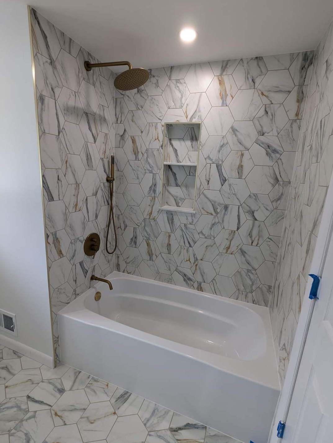 A newly renovated bathroom with a white tub, marble-patterned tiles, and bronze fixtures.