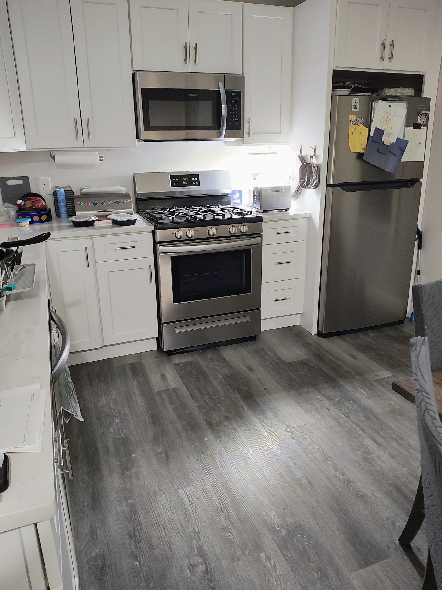 A kitchen with white cabinets, stainless steel appliances, and gray flooring.