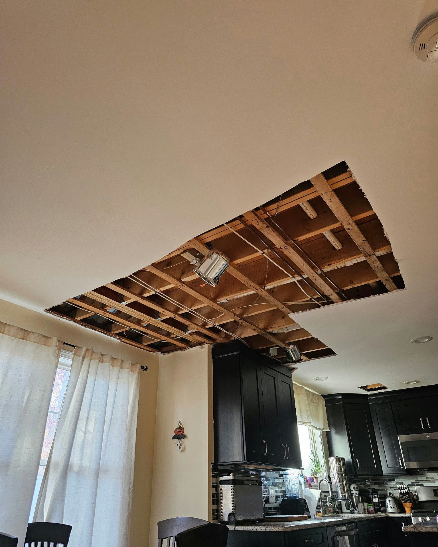 Ceiling with a large section missing, exposing wooden beams and electrical wiring.